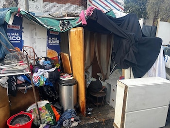 Una ranchada improvisada con lonas, cartones y objetos variados como ropa, un canasto, una jaula y publicidad de pan Bimbo en un espacio exterior