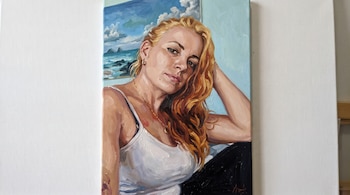 Pintura al óleo de una mujer de cabello rubio rojizo con camiseta blanca de tirantes junto a un cuadro marino.