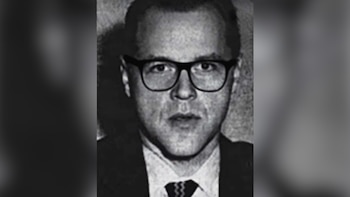 Retrato en blanco y negro de un hombre con gafas de montura negra, cabello oscuro, traje y corbata estampada, mirando al frente