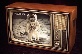 Un televisor antiguo de madera con una pantalla en blanco y negro que muestra a un astronauta del Apollo 11 parado en la superficie lunar.