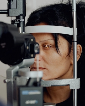 Mujer con cabello oscuro durante un examen ocular. Su cabeza está apoyada en un soporte y una lámpara de hendidura proyecta luz en su ojo