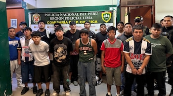 Grupo de hombres de pie en una comisaría frente a un cartel de la Policía Nacional del Perú y junto a dos agentes.