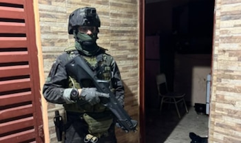 Un efectivo táctico con casco, uniforme y un arma de fuego permanece junto al ingreso de un inmueble