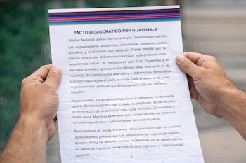 Dos manos sostienen una hoja de papel con el título "Pacto Democrático por Guatemala", que muestra texto impreso.