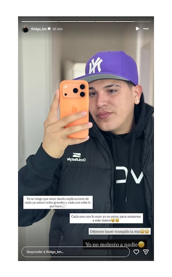 Thiago Medina se toma una selfie frente a un espejo, sosteniendo un smartphone naranja; viste gorra morada, buzo y campera negra, con texto superpuesto en la imagen