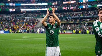 Un jugador de fútbol con camiseta verde y el número 19 aplaude sobre el césped de un estadio repleto de público.