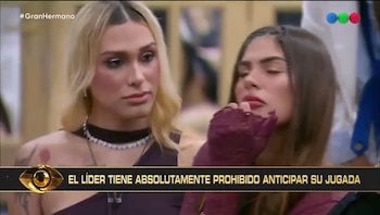 Dos mujeres, una rubia y una morena, aparecen en pantalla con expresiones serias mientras una barra inferior muestra el texto sobre la prohibición del líder en Gran Hermano