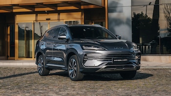 Un SUV oscuro BYD Seal U DM-i estacionado sobre un suelo empedrado, frente a un edificio con puertas de cristal y fachada dorada