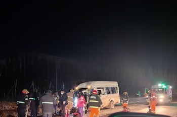 Vista nocturna de un accidente vehicular con una van blanca dañada en el arcén, rodeada por personal de emergencia y una ambulancia con luces