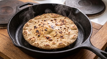 Un pan plano tostado despide vapor desde una sartén negra de hierro fundido colocada sobre una superficie de madera.
