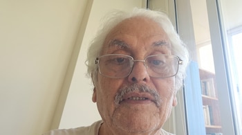 Primer plano de un hombre mayor con anteojos, cabello blanco y bigote, ubicado frente a una ventana.