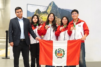 Cuatro estudiantes con chaquetas rojas y un adulto sostienen la bandera de Perú y muestran sus medallas frente a una imagen de Machu Picchu