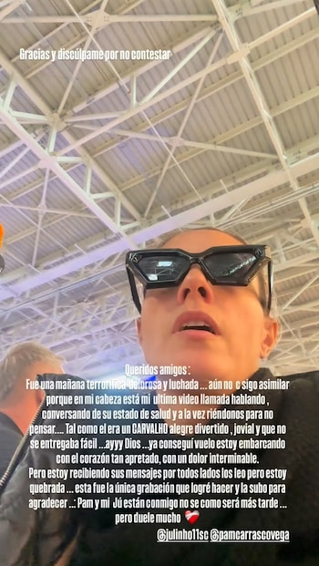 Primer plano de Brenda Carvalho, con gafas de sol oscuras y la boca ligeramente abierta, mostrando una expresión de tristeza. Se observa un techo de estructura metálica al fondo