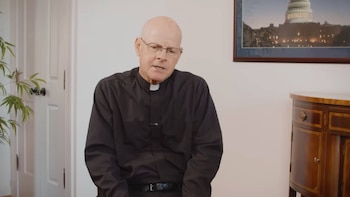 Un hombre calvo con gafas y camisa clerical negra habla, con una puerta blanca, una planta verde, un cuadro del Capitolio y un mueble de madera oscuro detrás