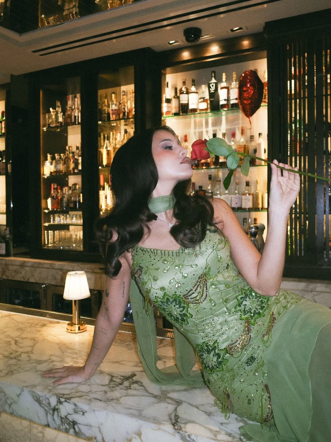 Emilia Mernes posa elegantemente en un bar con un vestido verde brillante y una rosa roja, durante su participación en la Semana de la Moda de Nueva York (Instagram)