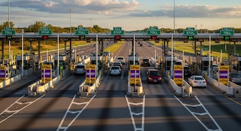Vista elevada de múltiples cabinas de peaje en una autopista de Estados Unidos con varios vehículos circulando bajo letreros de 'TOLL' y 'E-ZPass'.