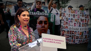 Mujer con vestido colorido habla en podio con el cartel "Plataforma de Transparencia para las Obras del Mundial". Manifestantes detrás sostienen pancartas de desaparecidos.