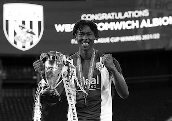 Fotografía en blanco y negro de un joven futbolista sonriendo mientras sostiene un trofeo con cintas y lleva una medalla al cuello