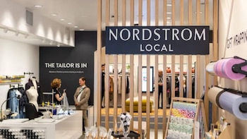 Interior de una tienda Nordstrom Local con un cartel central. Se observa una estación de sastrería a la izquierda y rollos de papel de regalo a la derecha