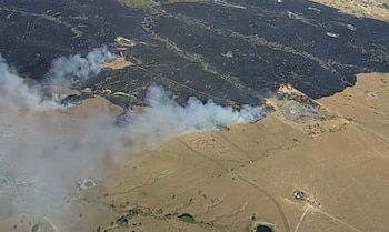 Vista aérea de un terreno dividido entre una zona quemada de color negro con humo blanco y un área de vegetación seca color café