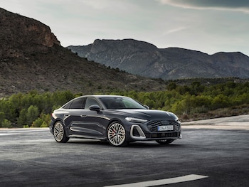 Automóvil Audi A5 2025 de color gris oscuro estacionado en una carretera asfaltada frente a montañas, árboles y cielo