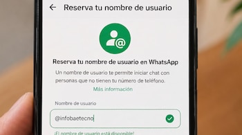 Mano sostiene teléfono móvil con pantalla que muestra la interfaz de WhatsApp para reservar nombre de usuario, icono de persona y arroba, y texto @infobaetecno.