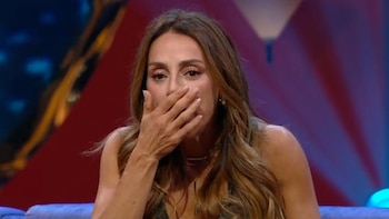 Eleonora Wexler con cabello castaño claro, cubriendo su boca con la mano derecha, con expresión de emoción. Fondo oscuro con luces rojas y azules