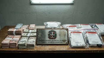 Mesa de evidencia policial de la DNCD en República Dominicana, con fajos de pesos dominicanos y dólares, placa de la DNCD y bolsas transparentes selladas con la etiqueta "DECOMISO".