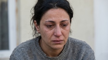 Un primer plano muestra el rostro de una mujer de piel clara y cabello oscuro, con lágrimas cayendo por sus ojos y mejillas, y un suéter gris.