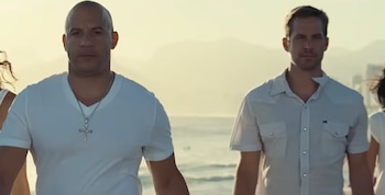 Vin Diesel y Paul Walker caminan en ropa blanca por una playa soleada con el mar de fondo