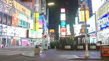 Vista nocturna de Times Square con grandes pantallas publicitarias iluminadas, edificios y una calle casi vacía, bajo un cielo oscuro