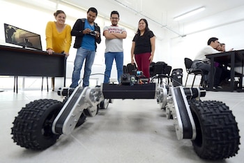 Cuatro estudiantes, dos hombres y dos mujeres, posan alrededor de un gran robot de ruedas robustas con una cámara, en un aula o laboratorio de la BUAP