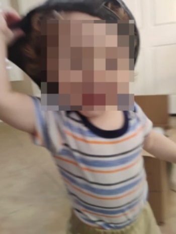 Un niño pequeño con cara pixelada, gorra oscura y camiseta a rayas azules, blancas y naranjas, y pantalones claros