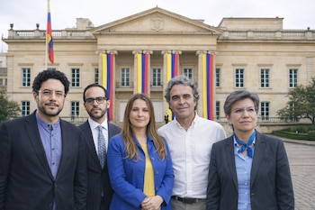 Cinco personas, tres hombres y dos mujeres, posan frente a la Casa de Nariño, un edificio claro adornado con los colores de la bandera colombiana.