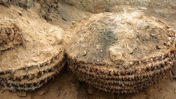Dos grandes estructuras semiesféricas de fibra vegetal trenzada y tierra, parcialmente expuestas en una excavación con terreno rocoso