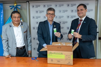 Tres hombres con traje y camisa posan junto a una caja de suplementos nutricionales, dos de ellos sujetan envases pequeños del producto