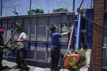 Hombres trabajando en la mejora de un portón de metal con alambre de púas en un día soleado. Un soldador y otro trabajador, con máquina de soldar naranja en primer plano