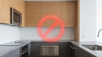 Una cocina moderna con gabinetes de madera clara, encimeras grises y electrodomésticos de acero inoxidable, con un gran círculo rojo brillante flotando en el centro.