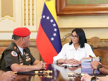 Delcy Rodríguez y un militar con boina roja conversan sentados a una mesa con la bandera de Venezuela al fondo