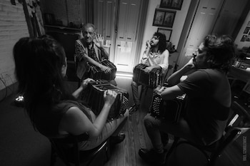 Fotografía en blanco y negro de cuatro músicos sentados en círculo con bandoneones. Un hombre mayor gesticula mientras tres personas más jóvenes los sostienen