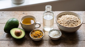 Palta entera y media, taza de té, cuenco con caléndula seca, cuenco con coco rallado, botella de aceite de coco, cuenco con avena.