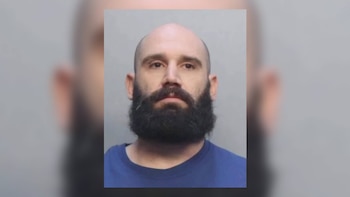 Retrato de frente de un hombre calvo con barba oscura y tupida, vestido con una camiseta azul, mirando directamente a la cámara