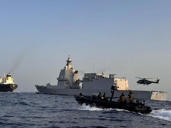 Un buque militar gris, una lancha con tripulación armada, un helicóptero y un petrolero en el mar bajo un cielo despejado
