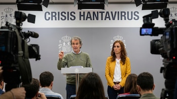 Un hombre en un podio con una mujer al lado, frente a un cartel que dice 'CRISIS HANTAVIRUS'. Hay cámaras y periodistas en primer plano.