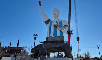 Vista de una enorme estatua de Lionel Messi vestido con la camiseta argentina, con el brazo levantado, frente a una multitud de personas con banderas