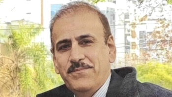 Primer plano de Mohsen Soltani Tehrani, un hombre de mediana edad con cabello oscuro y bigote, vistiendo una camisa a rayas y una chaqueta gris oscura