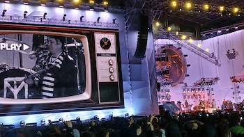 Gran pantalla de concierto con un diseño de televisor antiguo mostrando a Pity Álvarez en blanco y negro en un escenario, rodeado de luces y una multitud