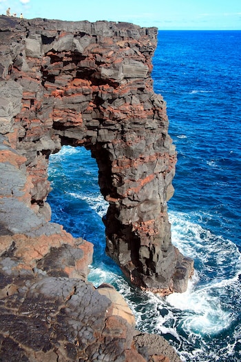 Un acantilado y un arco de roca volcánica oscura sobre el mar azul con espuma blanca