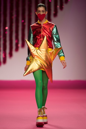 Ágatha Ruiz De La Prada en metalizados. Dos piezas: bomber tricolor, amarilla, roja y verde con mini falda amarilla con un enorme aplique de estrella dorada. Un look con sello 100% Ágatha. En sus pies, zapatillas con plataformas de goma de color y leggings de color verde