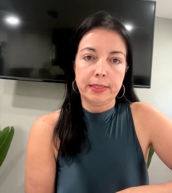 Mujer de cabello negro y pendientes redondos viste una blusa sin mangas frente a una pantalla de televisión